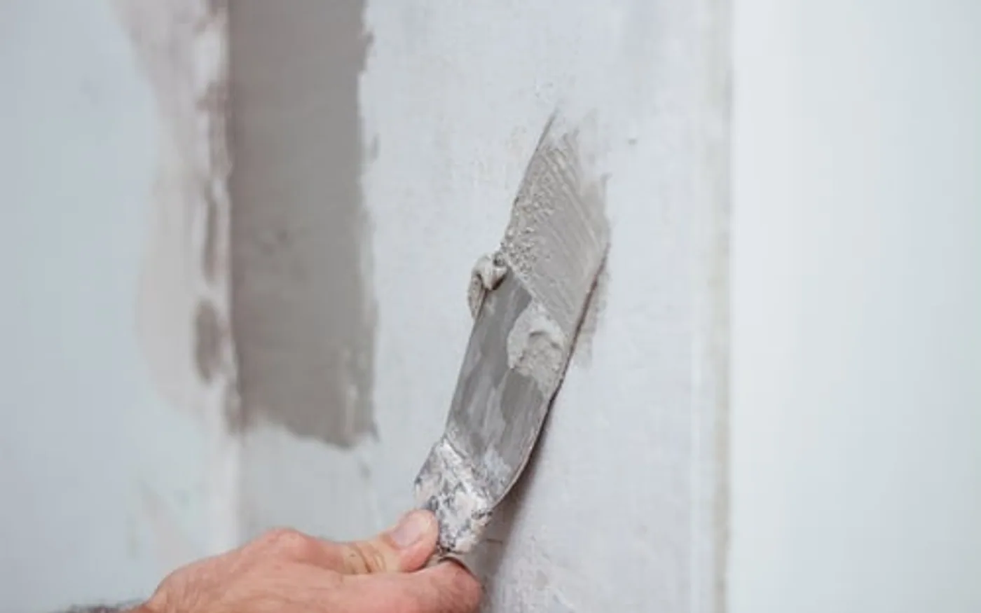Taping knife smoothing joint compound over a repaired drywall seam on an interior wall
