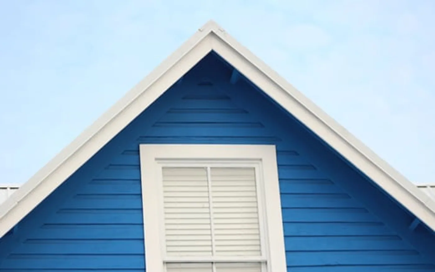 Freshly painted blue exterior siding and white window trim on a home gable under clear sky