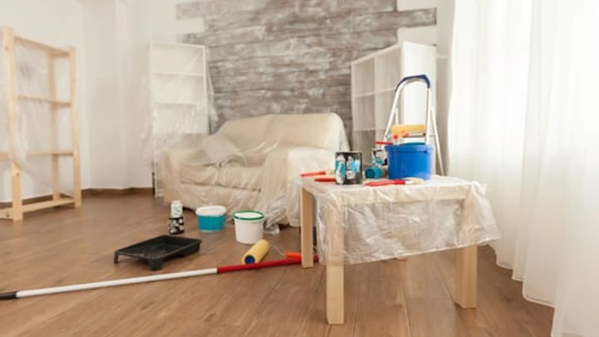 Living room mid-repaint with drop cloths, ladder and paint supplies on site
